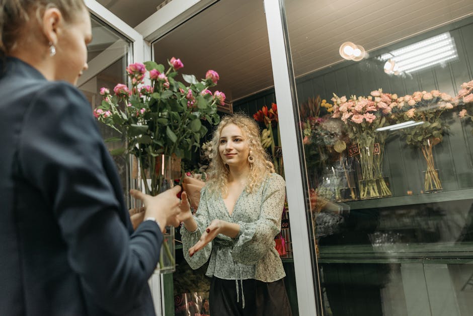 A florist from FloristhonoRoak is handing a bouquet of pink roses wrapped in brown paper to a customer inside a flower shop near Honor Oak Park station. The bouquet features fresh, vibrant pink roses 
